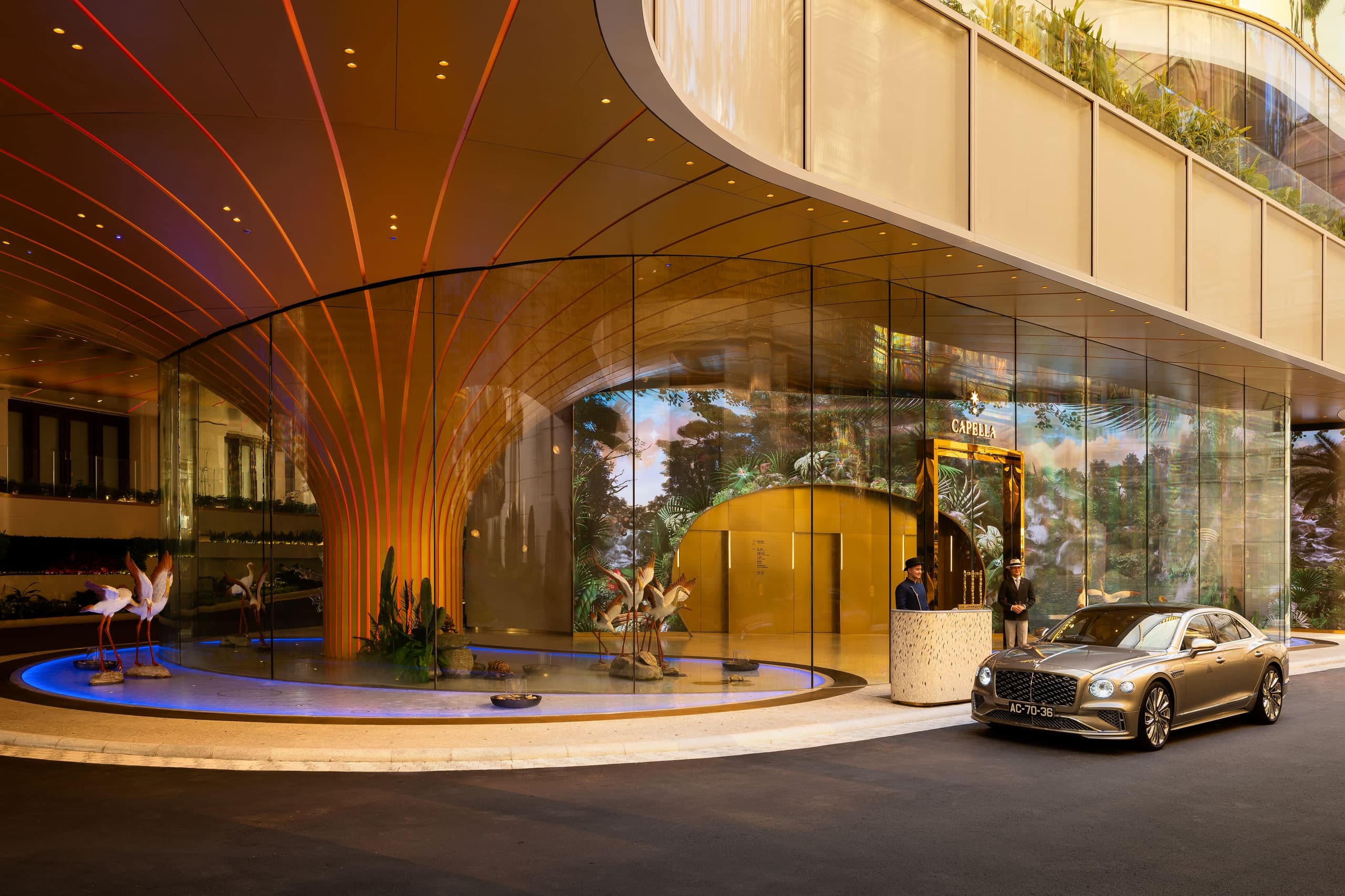 Night arrival at Capella at Galaxy Macau with gold Capella signage, Tree of Life lobby structure, and a Bentley at the porte-cochère